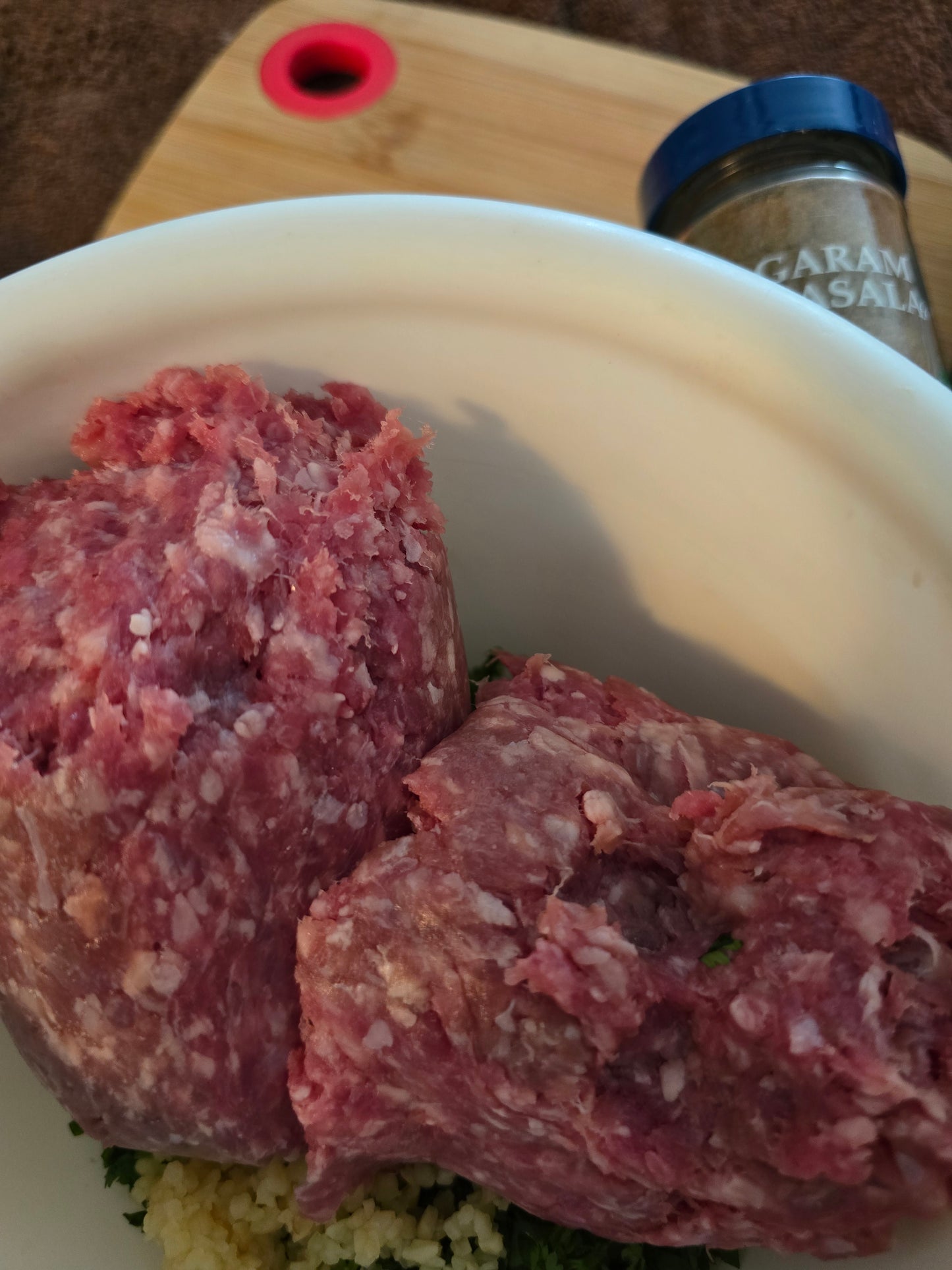 Raw ground goat meat in a white bowl with a bottle of seasoning in the background.