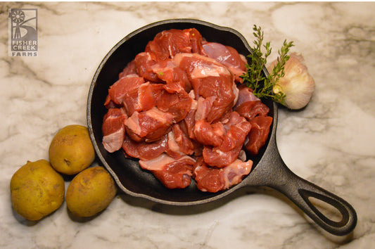 goat stew meat in cast iron with potatoes, thyme and bulb of garlic. Branded Fisher Creek Farms