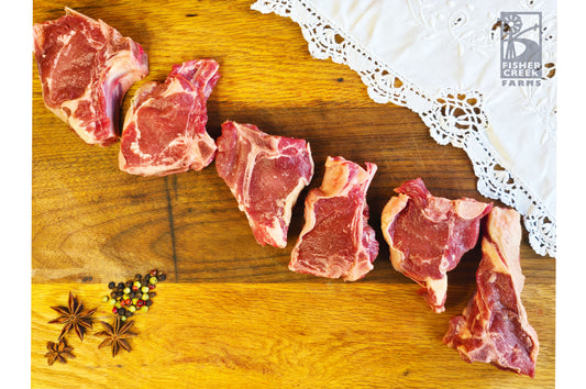 Goat chops on a wooden cutting board with a lace cloth and spices.
