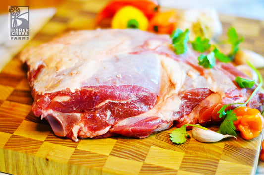 Goat shoulder roast on a wooden cutting board with peppers, spices and a brand logo in the corner.